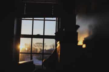 Man sitting alone inside dark room with sun shining through window.